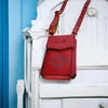 Red leather crossbody bag with studded details on a white decorative chair against a blue wall.