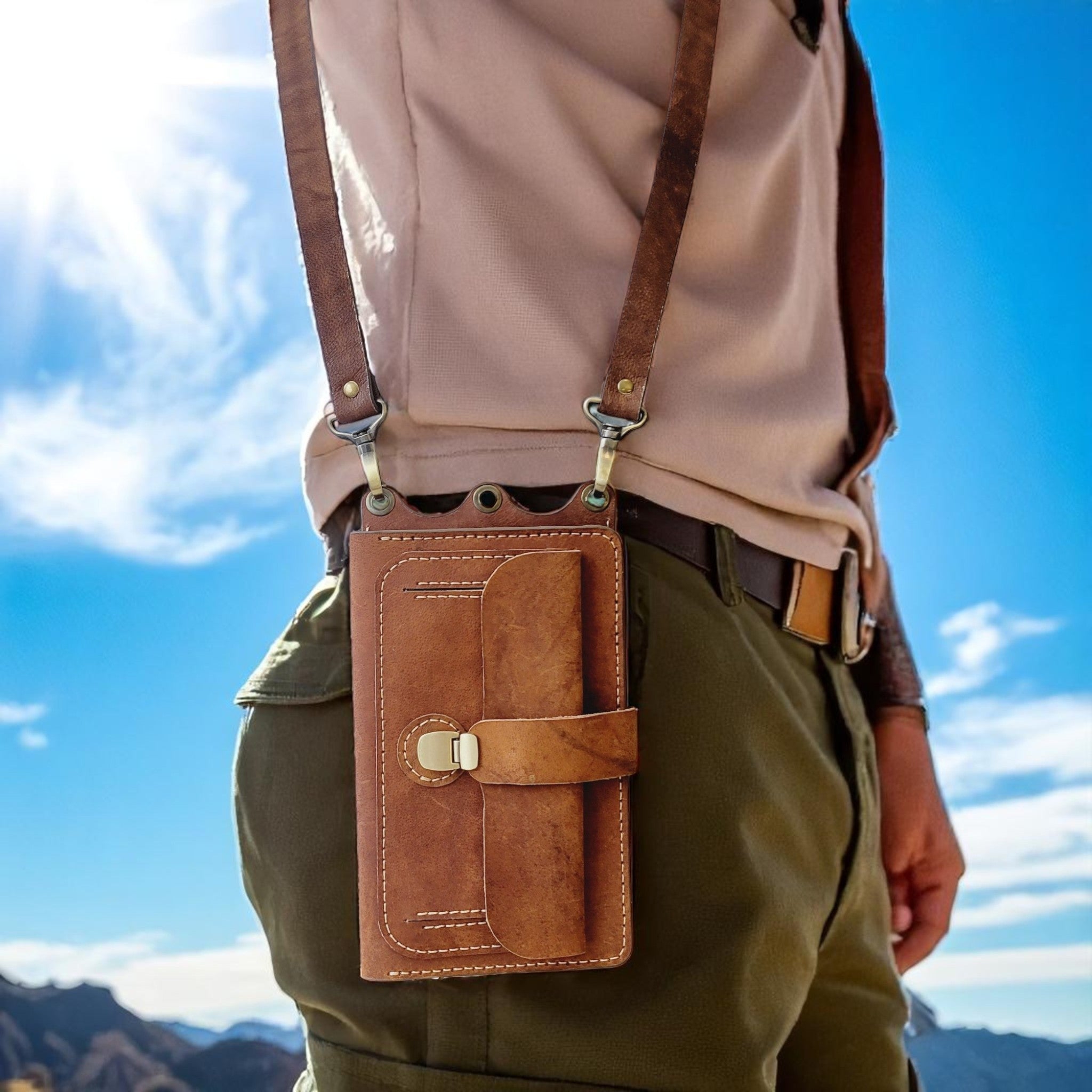 Person wearing a brown leather crossbody bag with a blue sky and mountains in the background