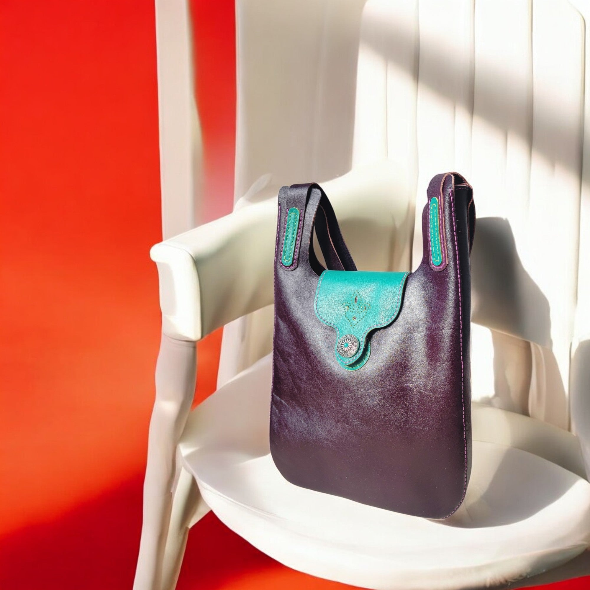 “Fioréa shoulder bag in eggplant leather with green stitching and a sculptural metal clasp (about 31×30×6 cm).”
