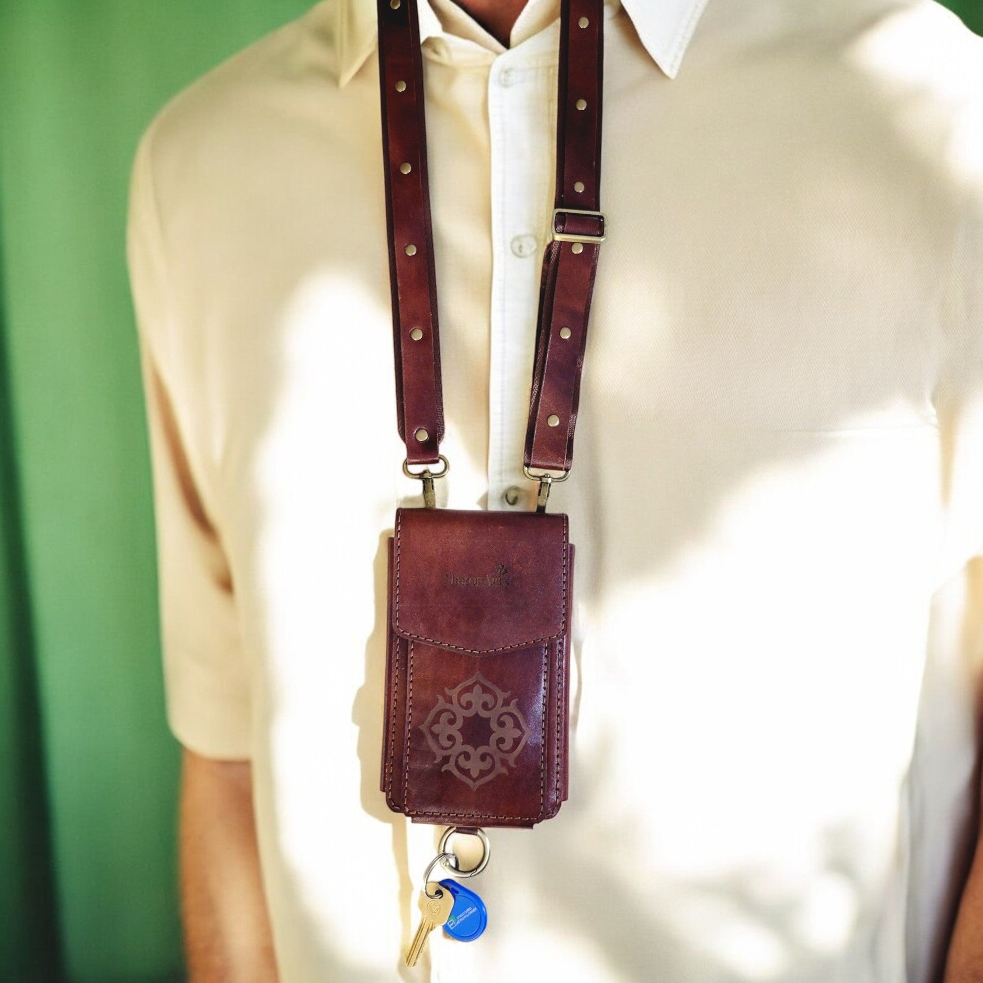 A compact brown leather passport bag with an adjustable strap and a keyring at the bottom, being worn around the neck.