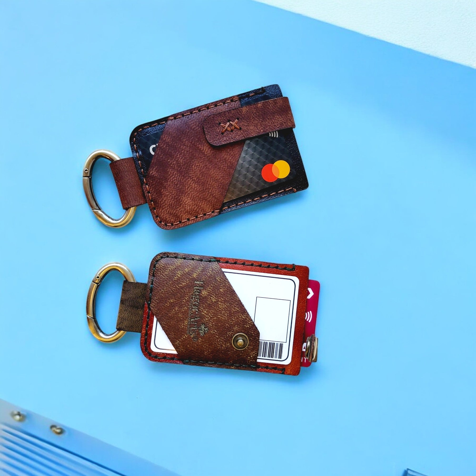 A brown leather card and key holder placed on a surface with a cityscape in the background.