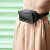 Person wearing a black waist bag on a beige outfit with a green background