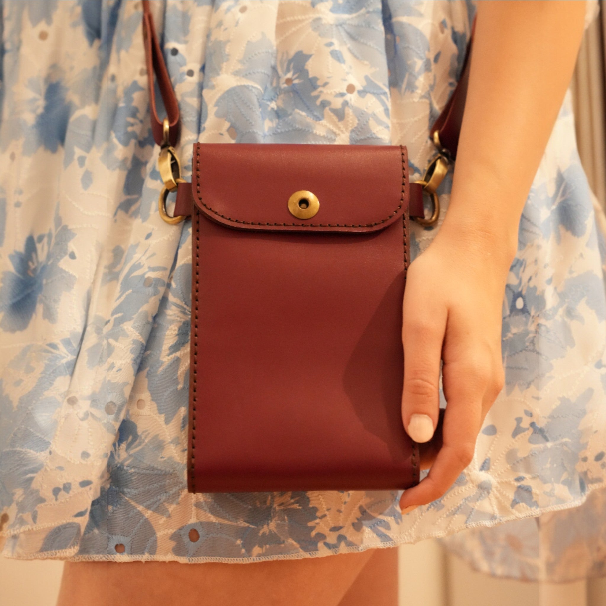 Brown leather pouch held by a person wearing a floral dress.