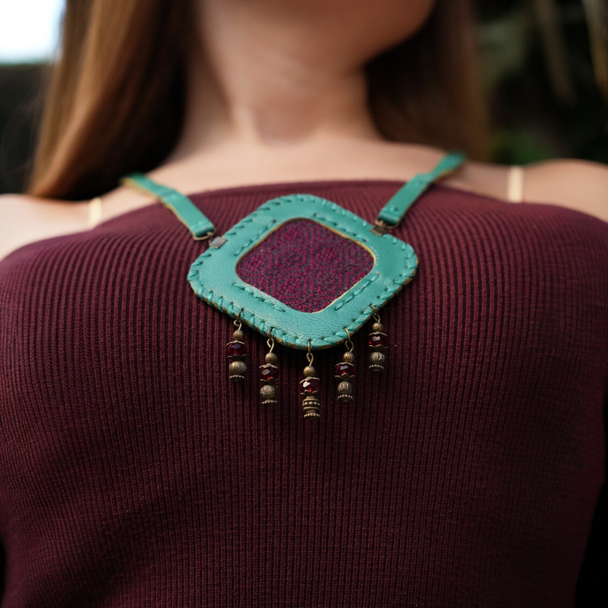 Person wearing a turquoise leather shoulder bag with decorative elements.