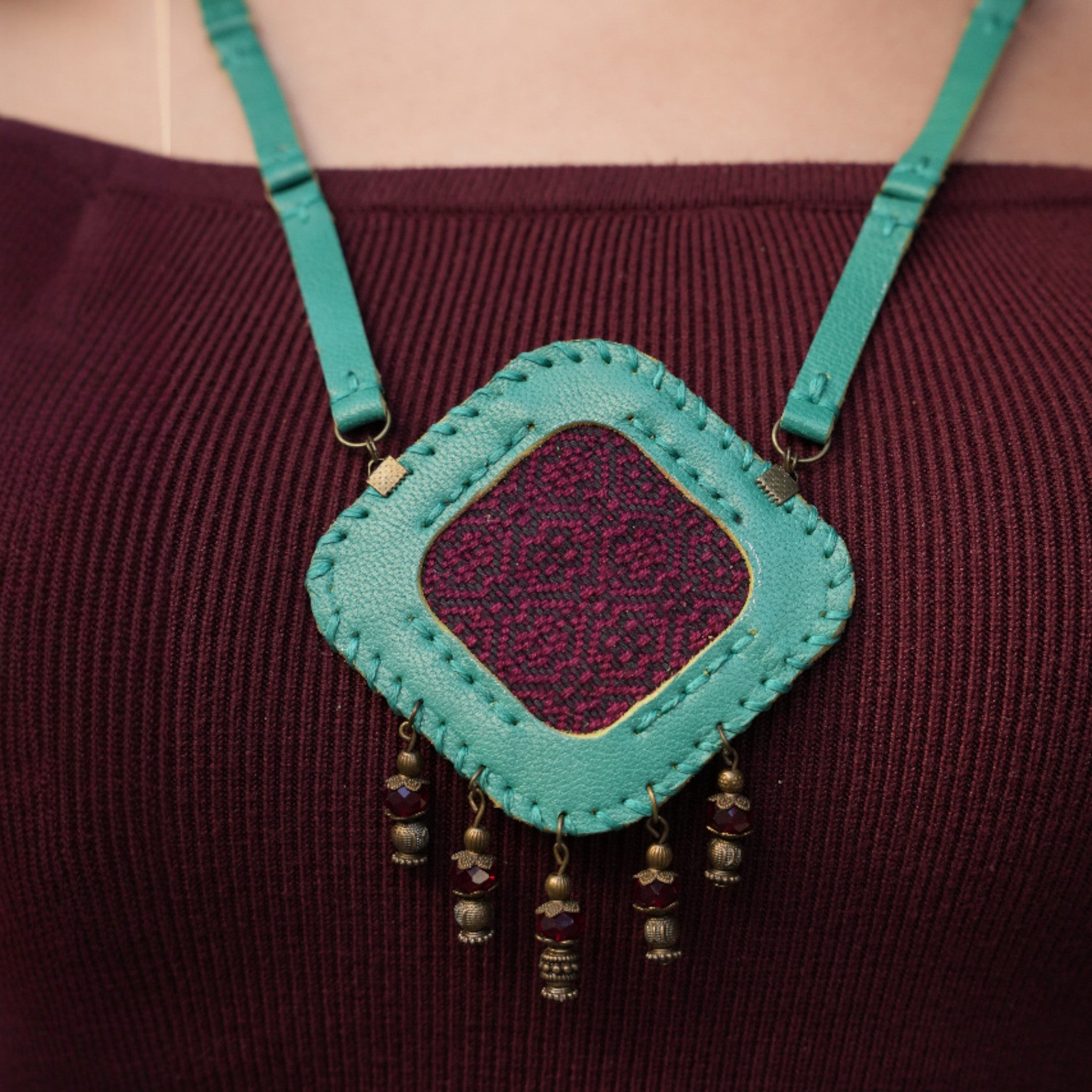 Turquoise leather purse with purple interior and bead decorations on a maroon background