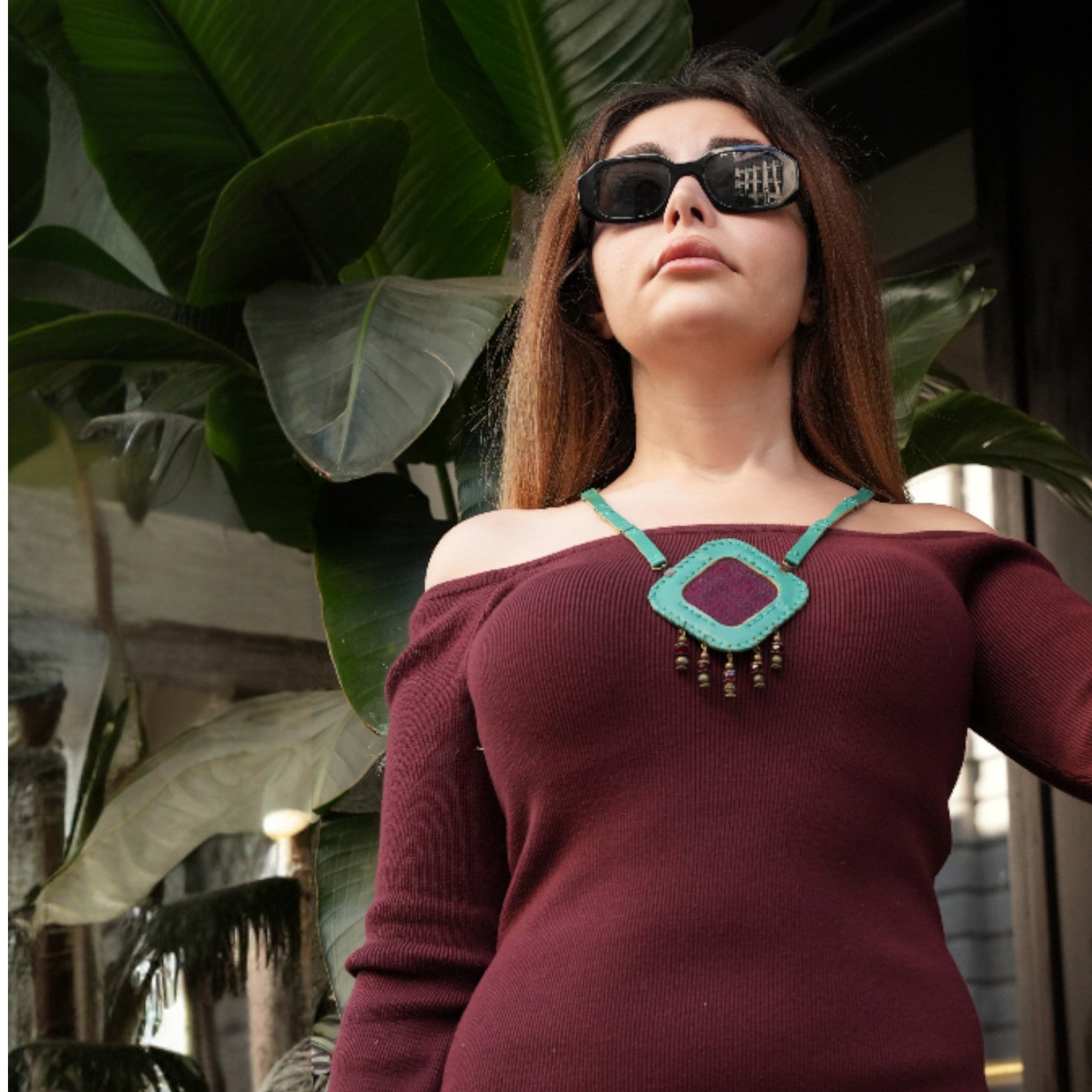 Woman wearing sunglasses and a burgundy top with a green necklace in an outdoor setting