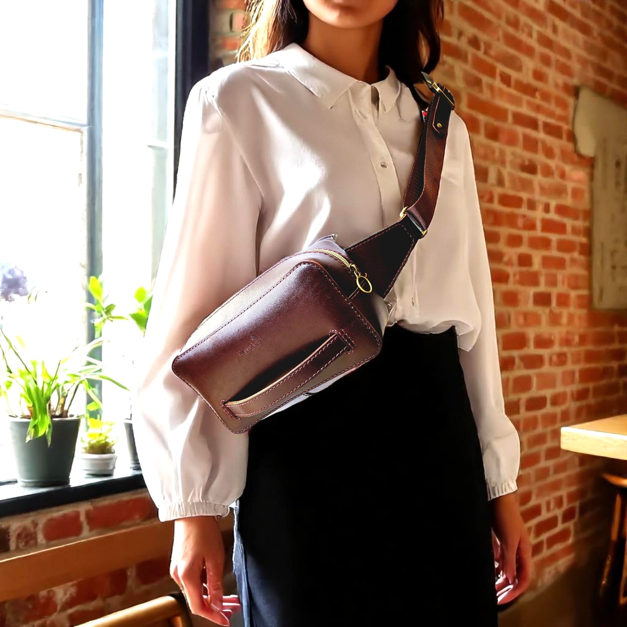 Person wearing a white shirt and dark pants with a brown leather bag over one shoulder, standing in a room with brick walls and plants.