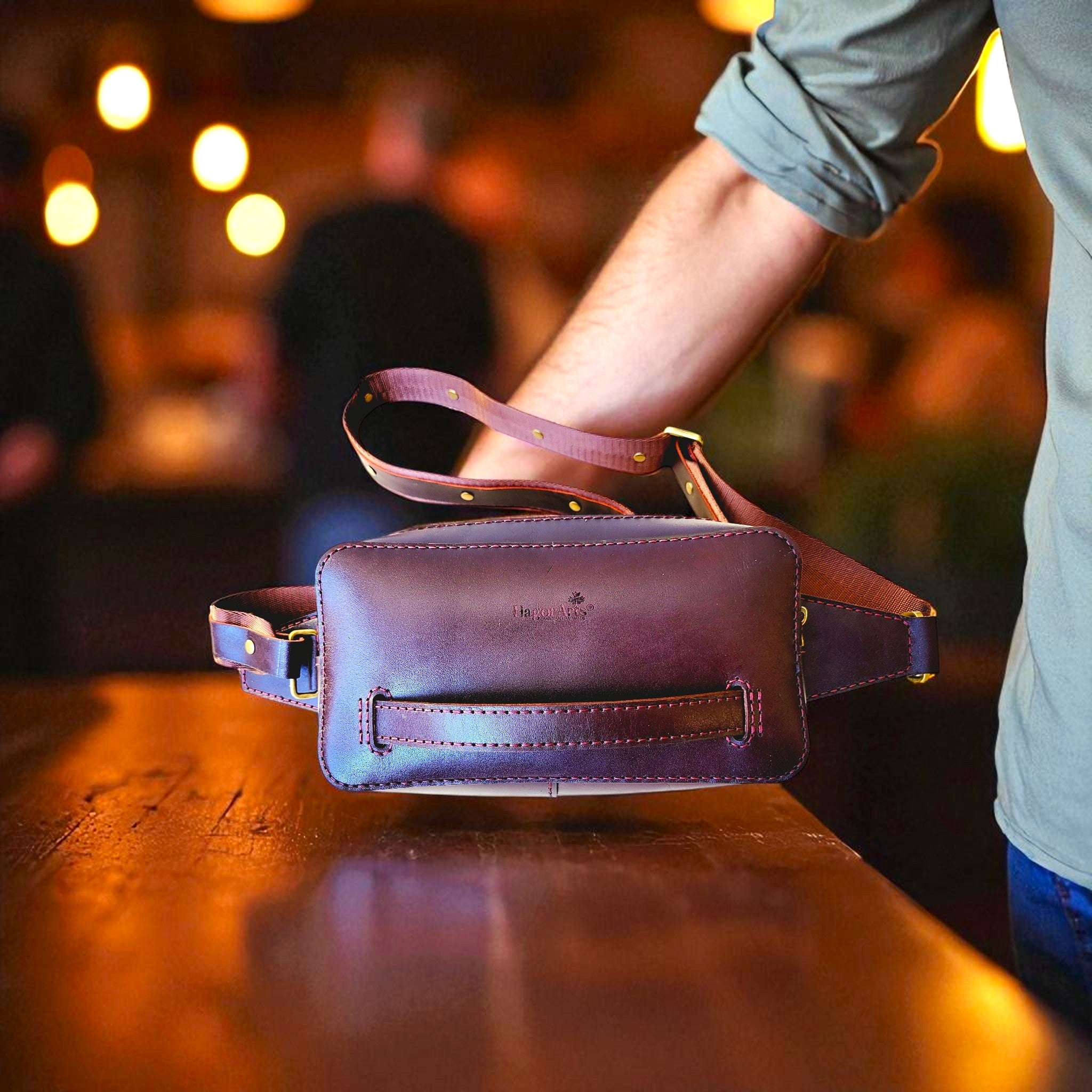 Brown leather waist bag on a wooden surface with a blurred background