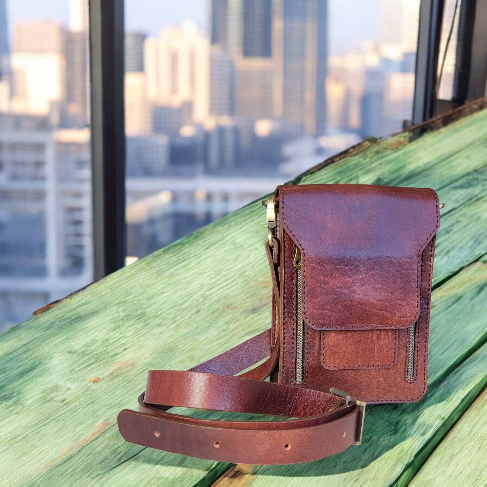 A red leather crossbody bag with multiple compartments and secure zippers, displayed on a wooden bench.