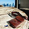 Brown leather wallet with strap on a wooden surface with city skyline in the background