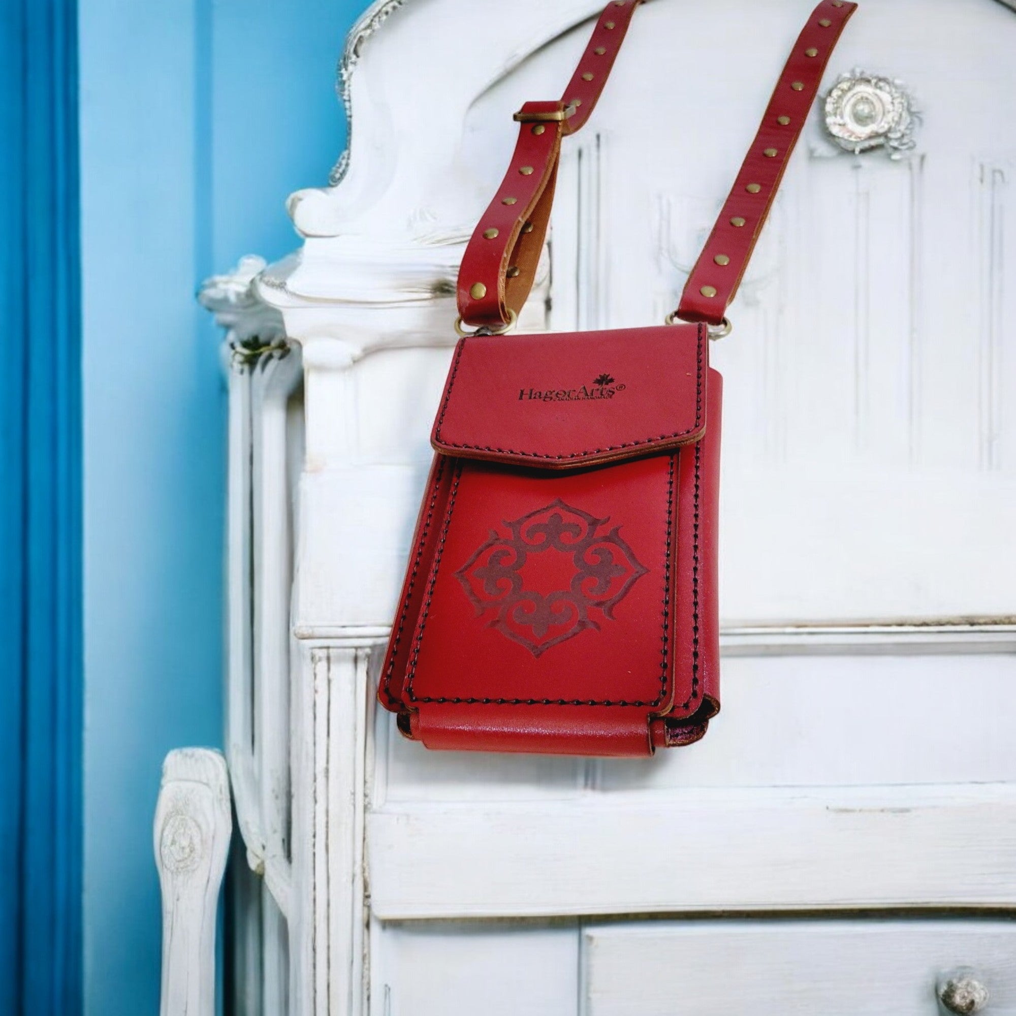Red leather crossbody bag with studded details on a white decorative chair against a blue wall.