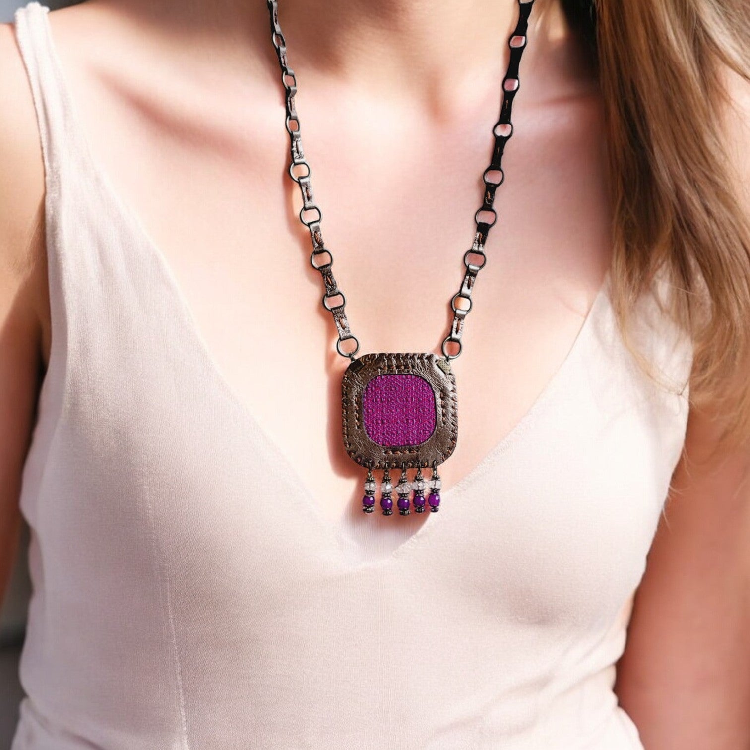 A person wearing a smoky glossy leather and vibrant purple fabric necklace with metal chains and dangling beads.