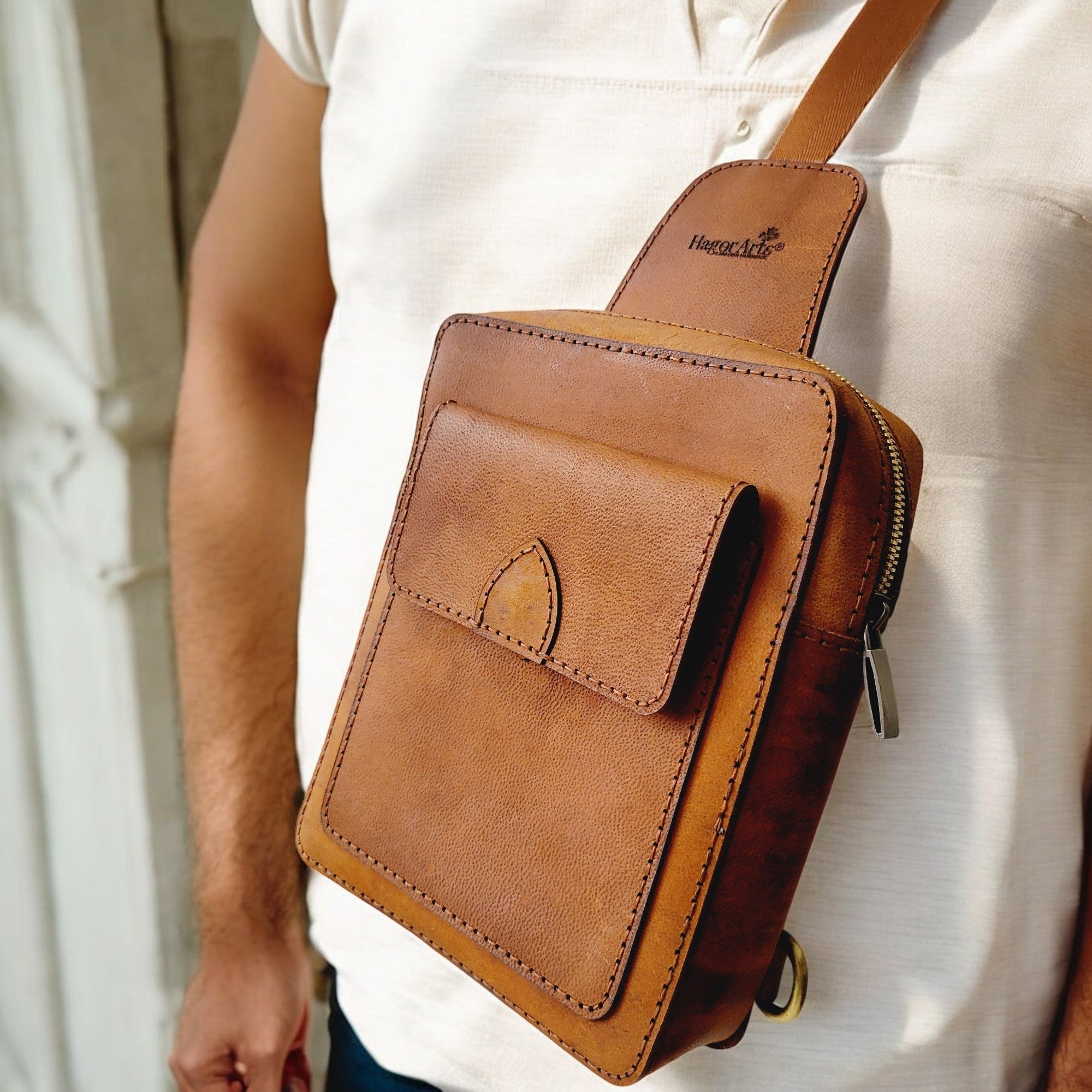 A person wearing a tan leather sling bag from the Odyssey Collection by HagorArts.