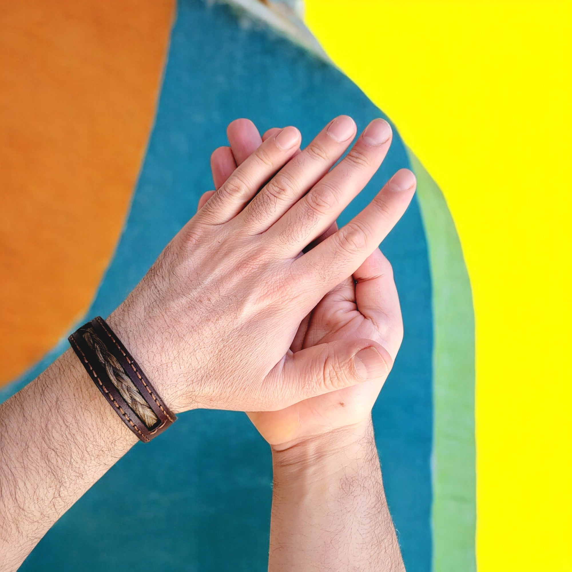 A person's hands showing a bracelet with a leather strap and a strand of hair, indicating a personalized and sentimental gift.