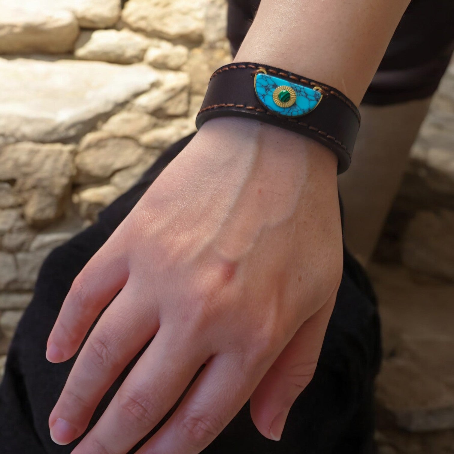 Close-up of a hand wearing the Orbis M1 leather bracelet in dark full-grain leather, featuring a distinctive handcrafted centerpiece and fine hand-stitched detailing.