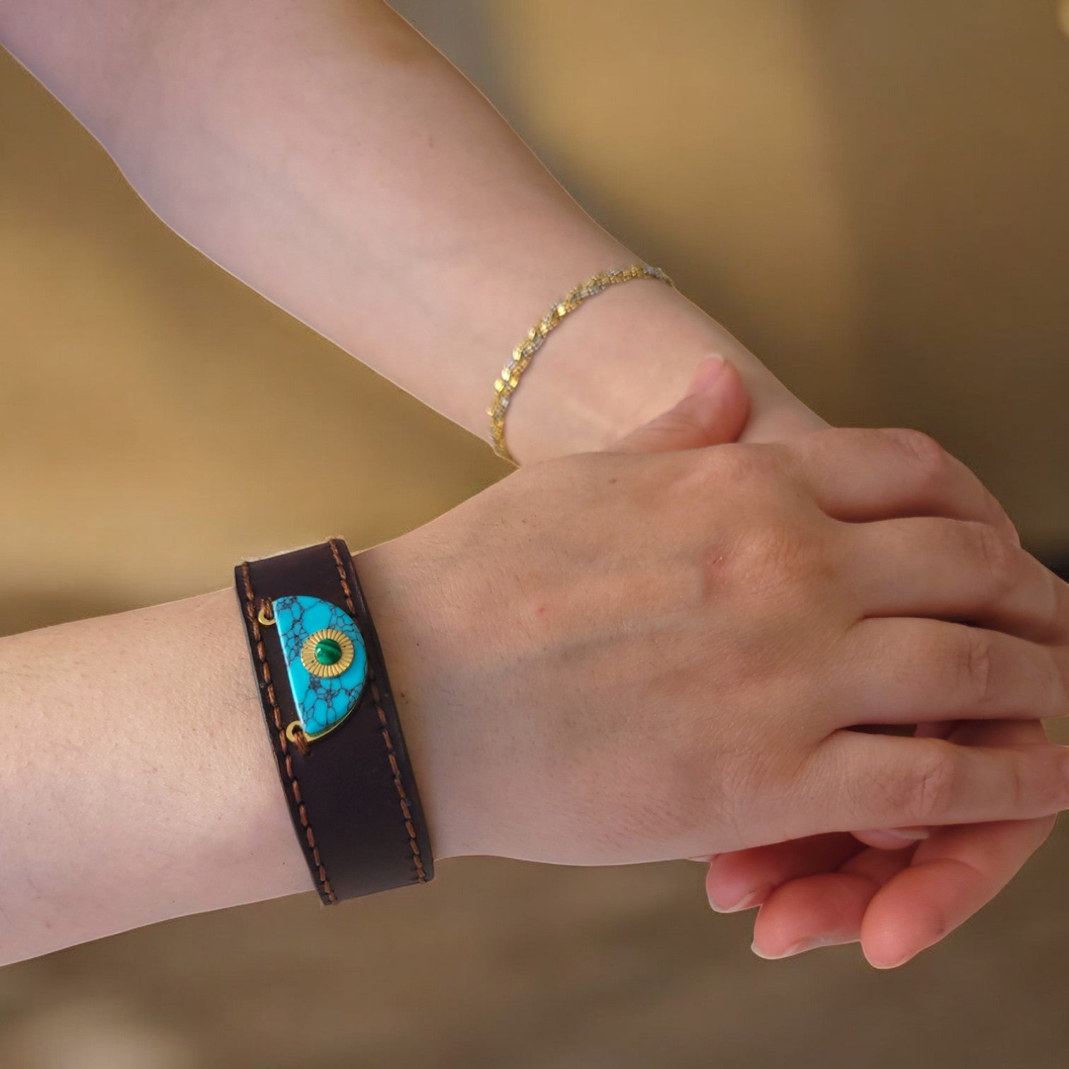 A person wearing a brown leather bracelet with a central blue stone.
