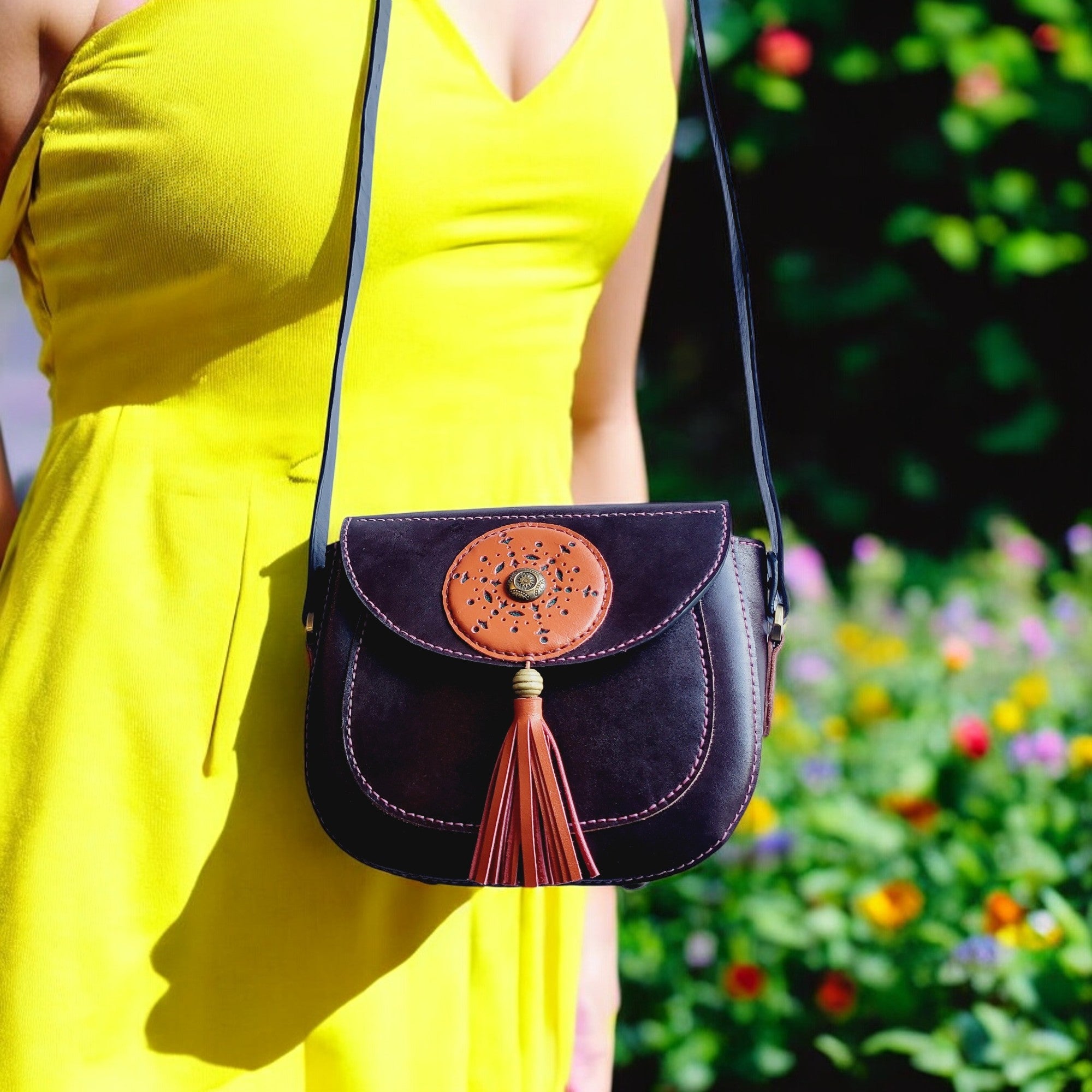 A person wearing a yellow dress is carrying a brown leather shoulder bag with an orange leather accent and a tassel hanging from it.