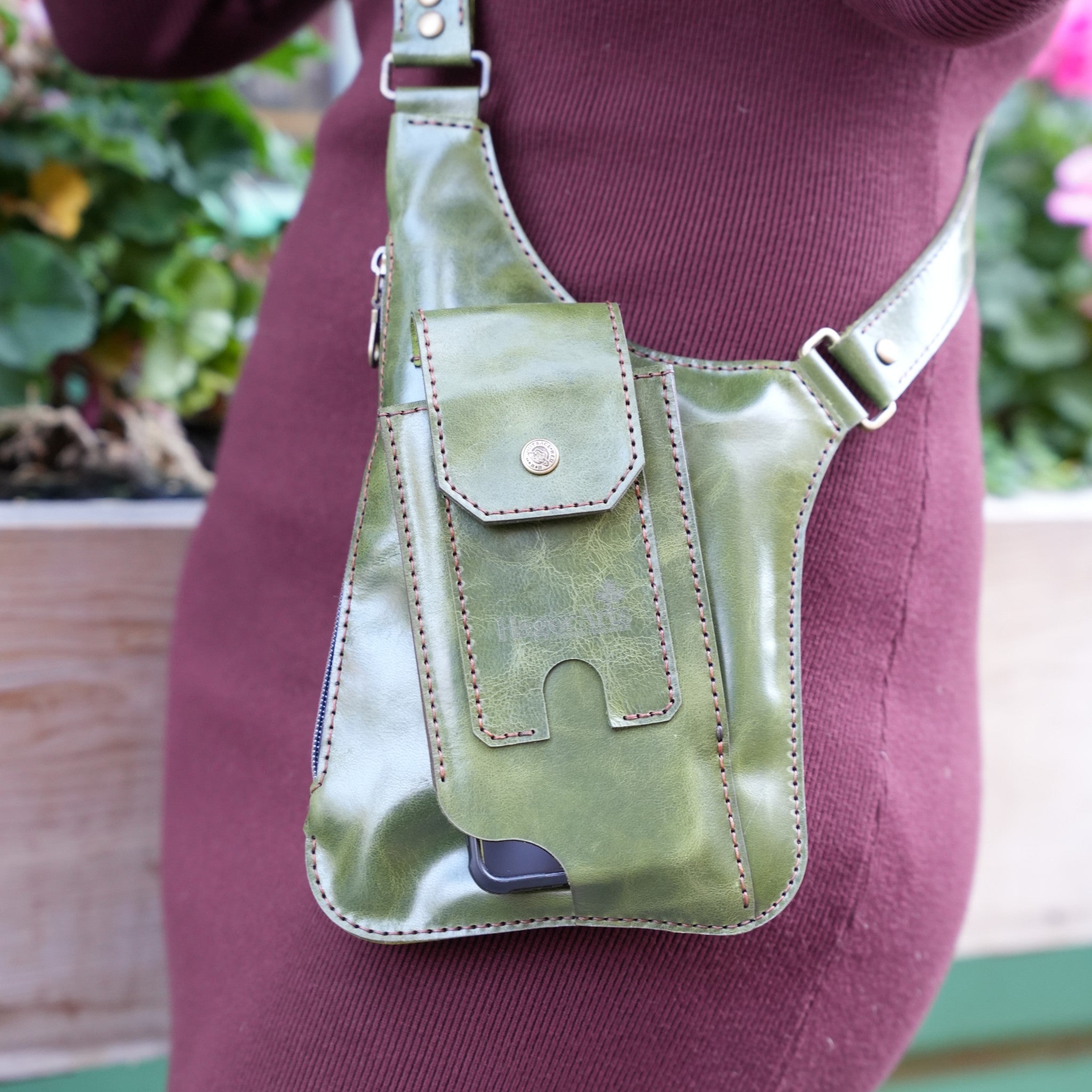 Green leather crossbody bag worn by a person with a blurred background
