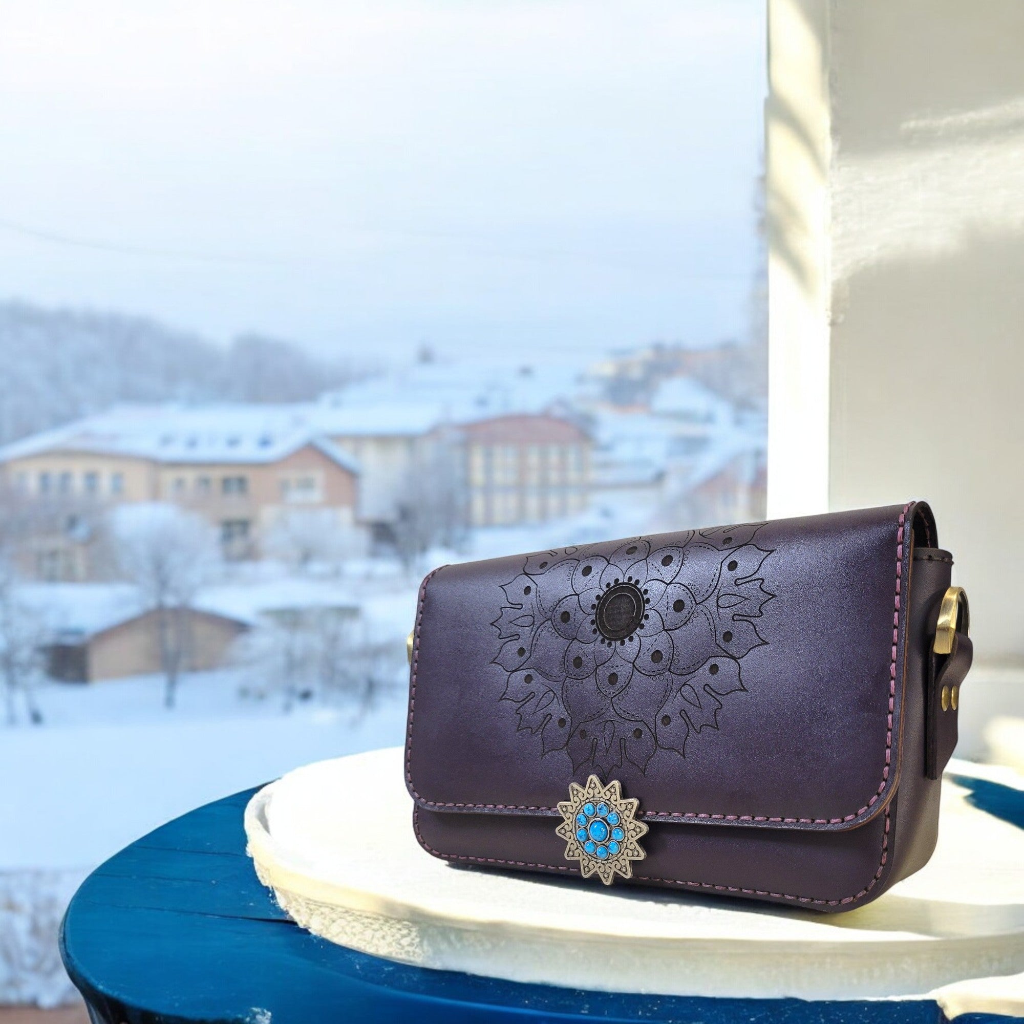 “Violet full-grain leather bag with turquoise-embellished floral clasp.”
